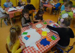 Piątka dzieci wycina z papieru elementy, które nakleja na kontur mapy Polski.